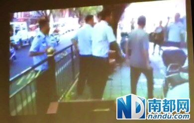  老胡来到铁栏杆前，试图翻越铁栏杆把凳子拿回来，被执法队员拽了回去。视频截图 南都记者 田飞翻拍